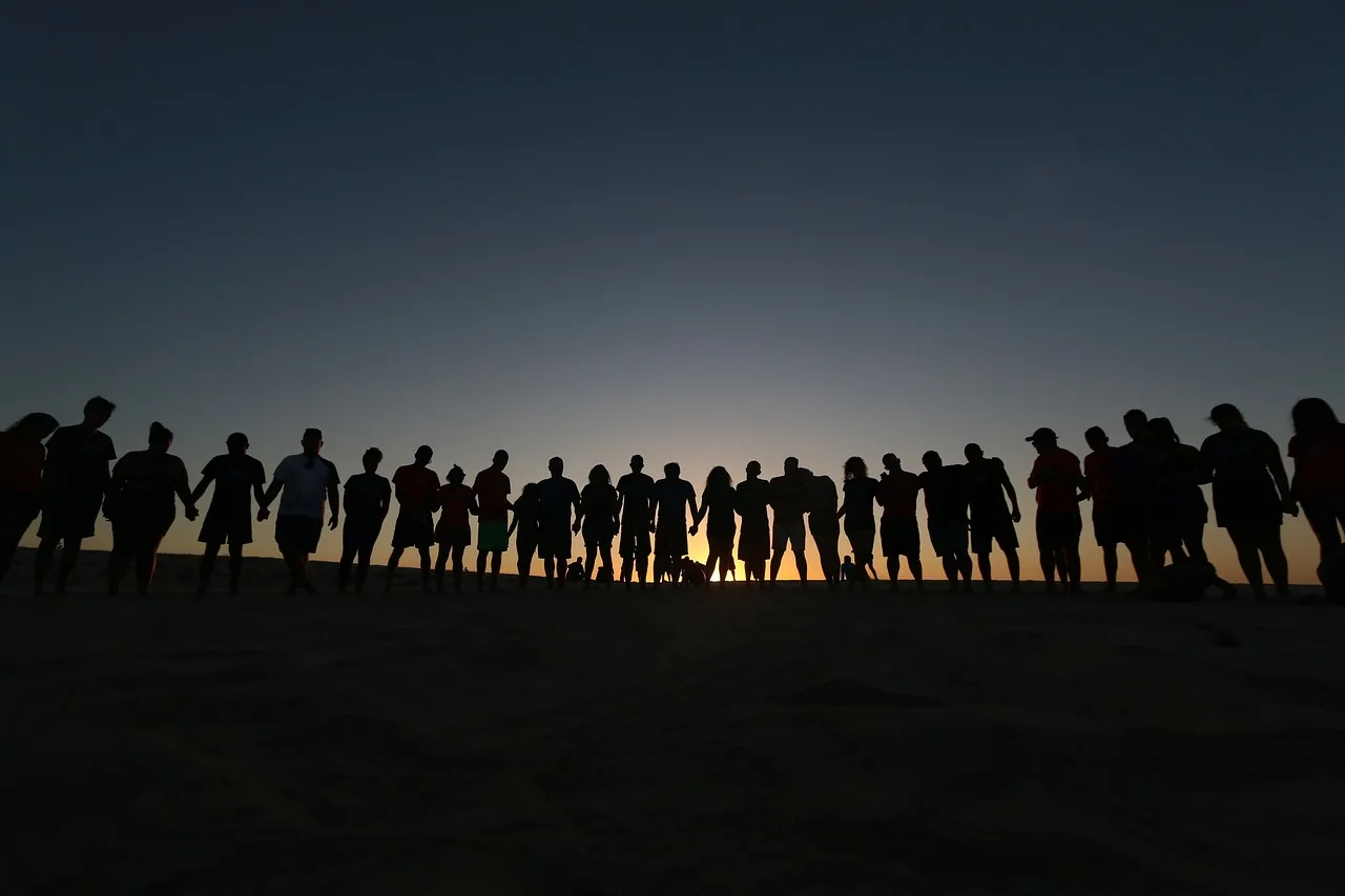 silhouette of people standing in a line with a sunset behind them